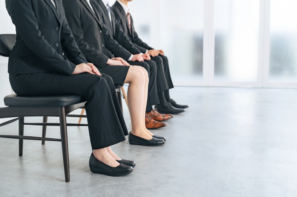 photo of 4 Japanese people in dark suits, legs only, waiting for a recruitment interview